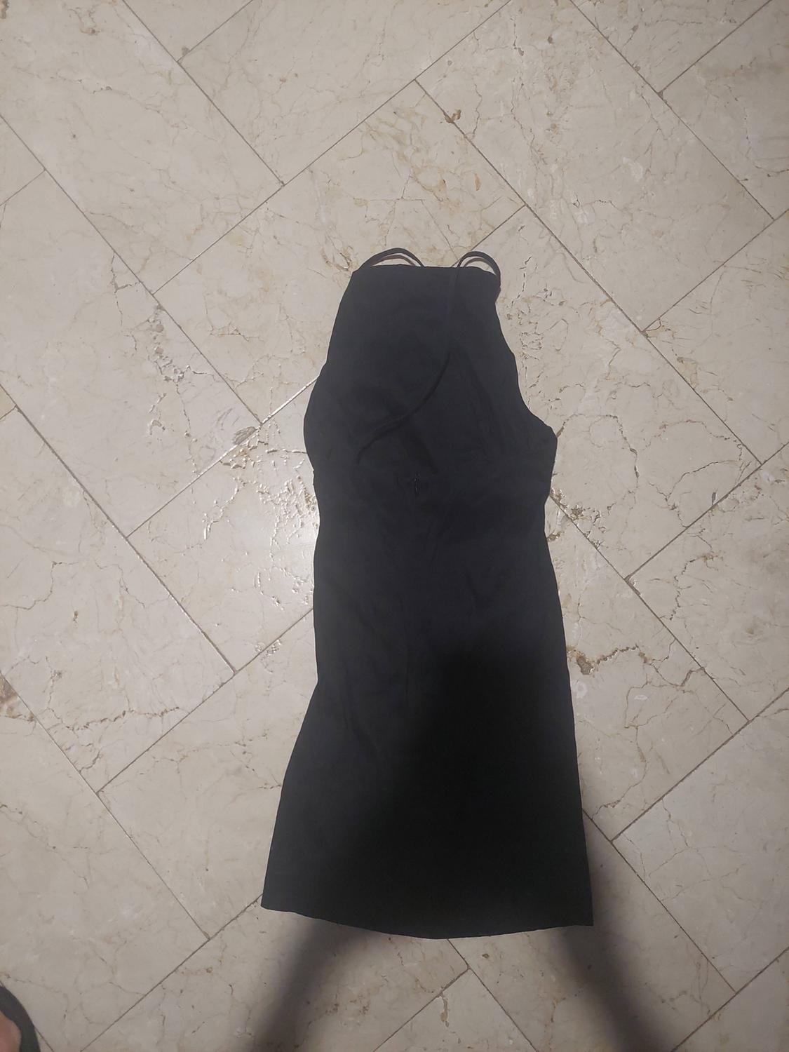 Short black sleeveless dress laid out on a light-coloured tiled floor. Viewed from above with shadows at the bottom.