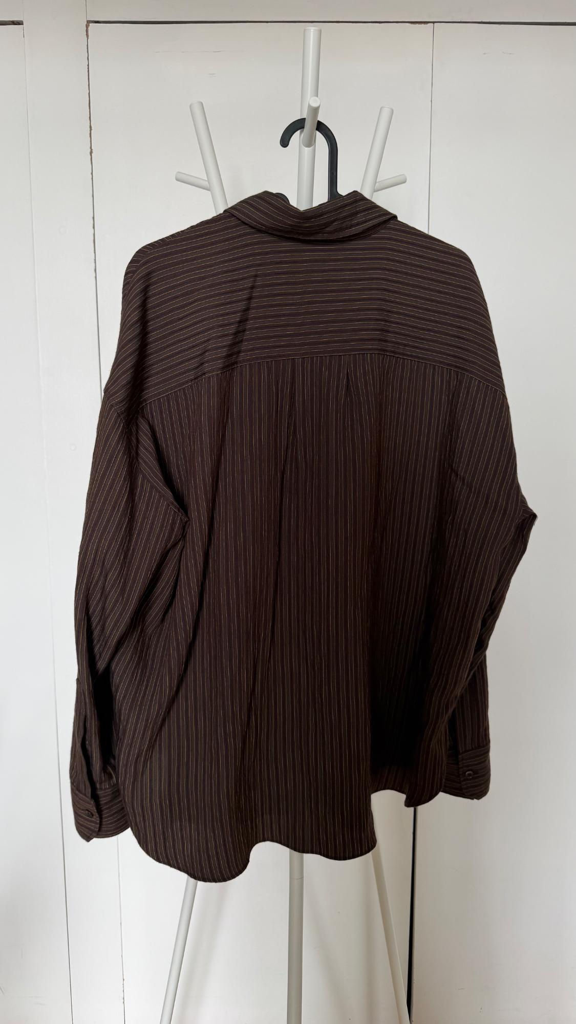 Rear view of a dark brown, pinstriped shirt hanging on a white coat rack in front of white doors.