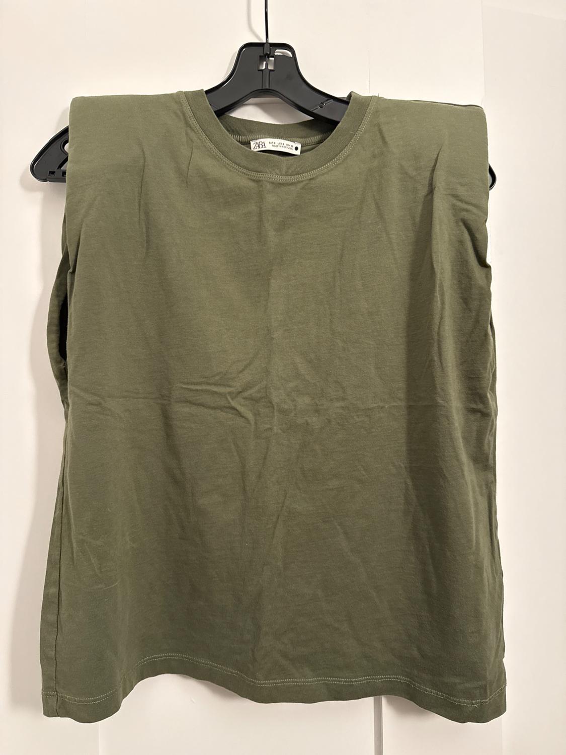Olive green t-shirt hanging on a black hanger against a white background. The visible tag shows the brand.
