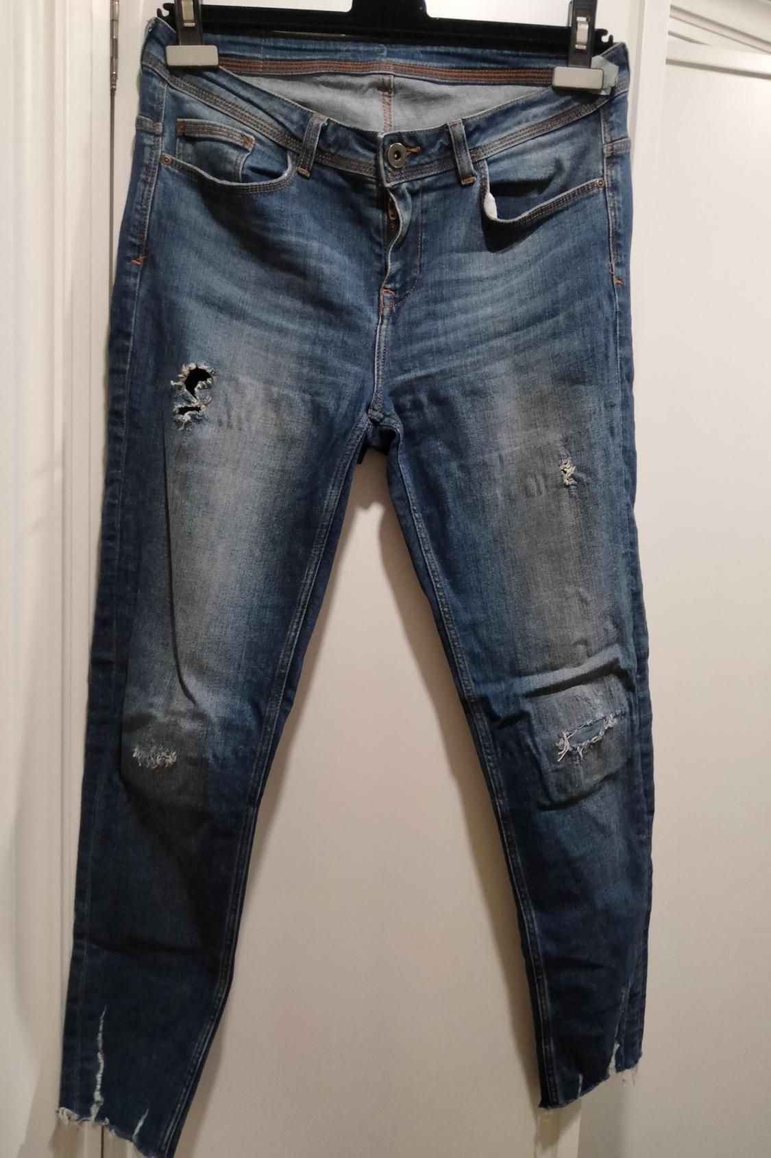 Front view of distressed denim jeans with front pockets and rips on the legs.