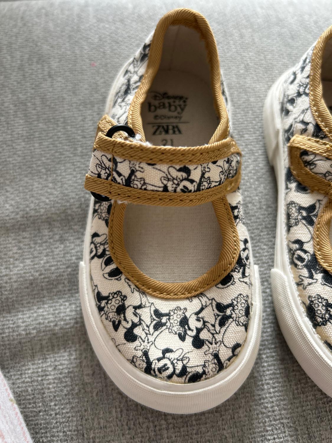 Kids' shoes with black and white Disney character print, yellow trim, and white sole. Visible text: "Disney baby ZARA 21".