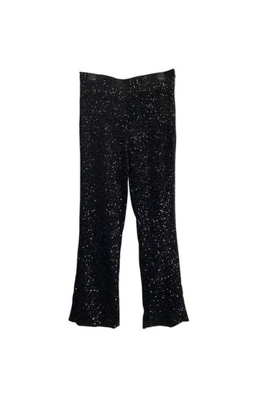 Black trousers with sparkly sequins hanging against a white backdrop.