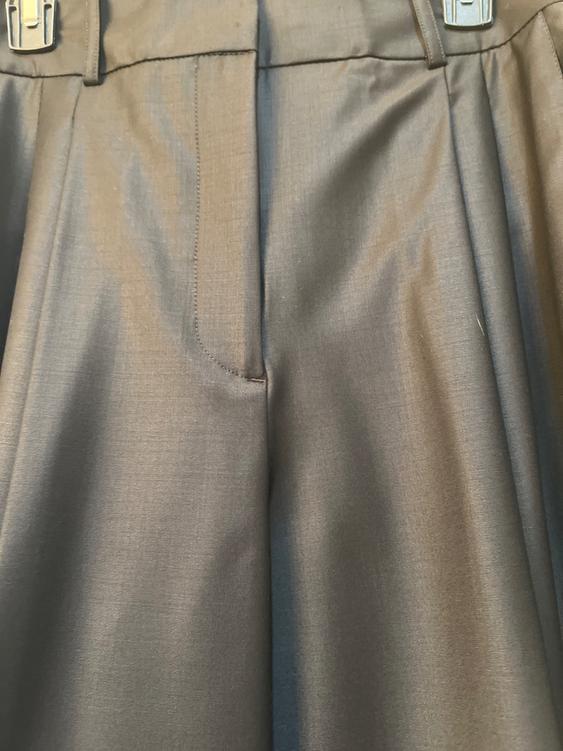 Gray plain fabric trousers with pleats and a waistband with visible metallic buckles at the top.