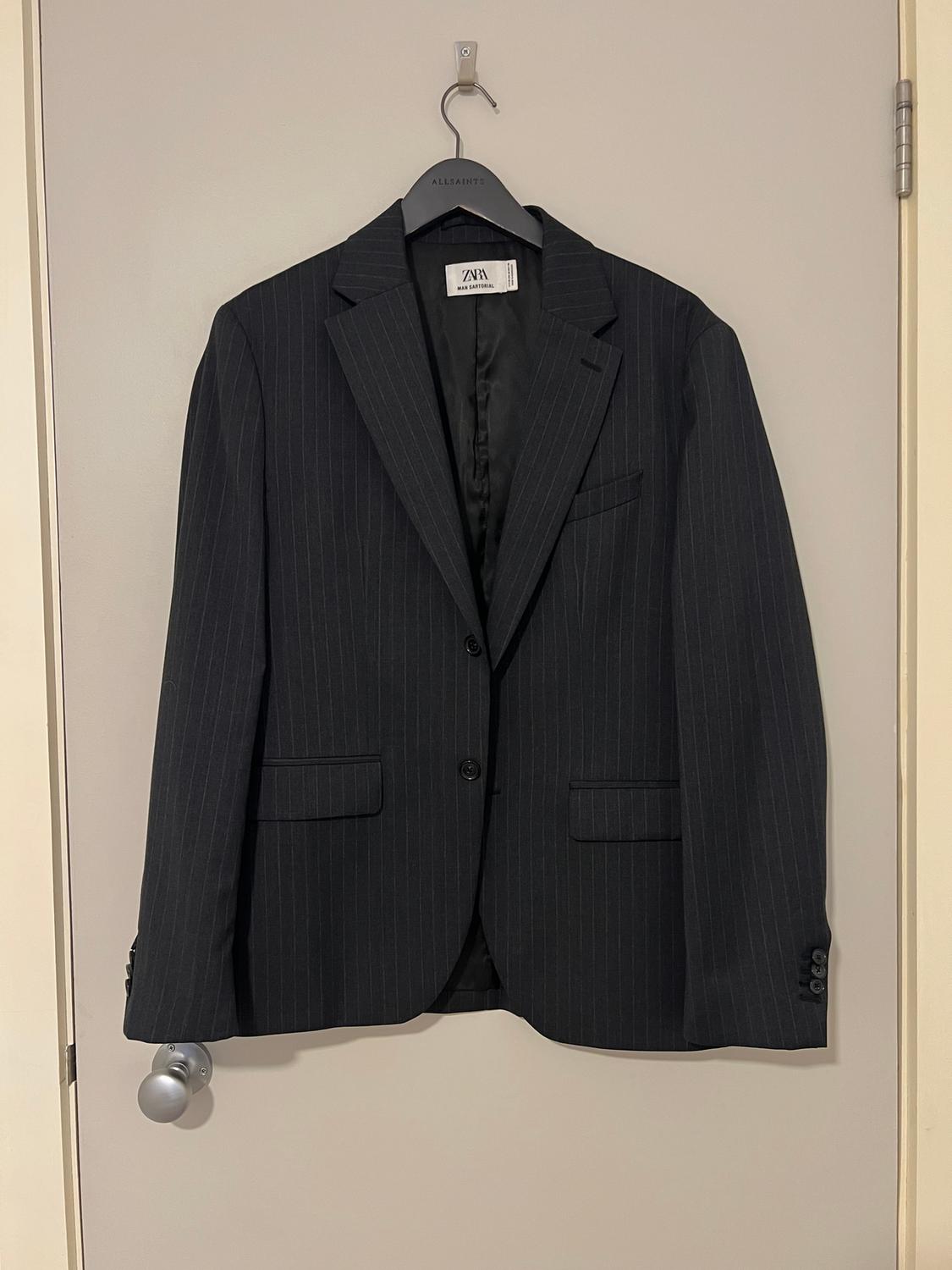 Black pinstripe jacket hanging on an AllSaints hanger over a beige door. Visible label: Zara Man Edition.