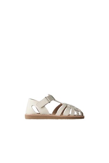 Side view of beige sandal with interwoven straps and brown sole.