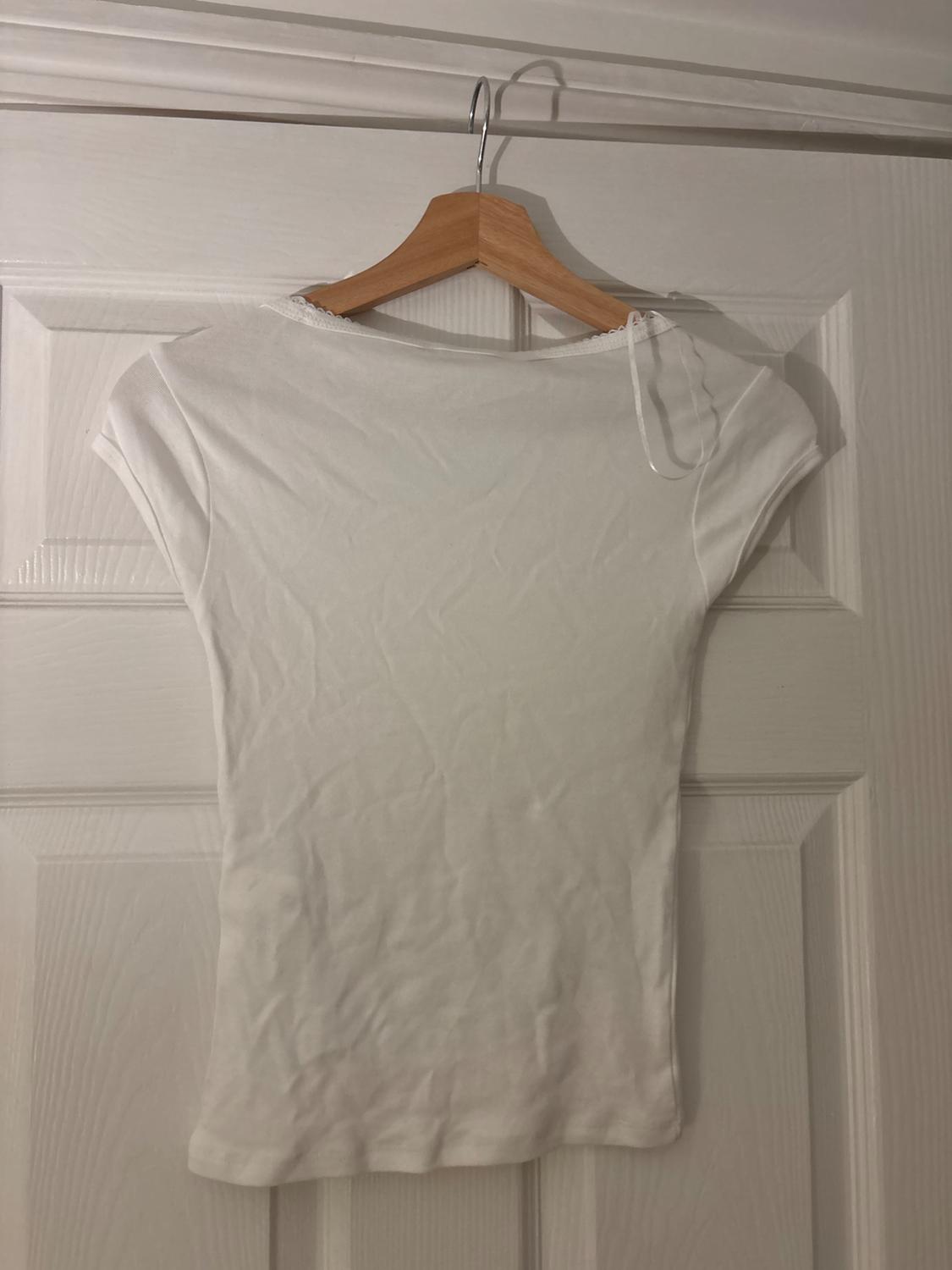 White short-sleeved t-shirt hanging on a wooden hanger over a white door. The fabric is slightly creased.