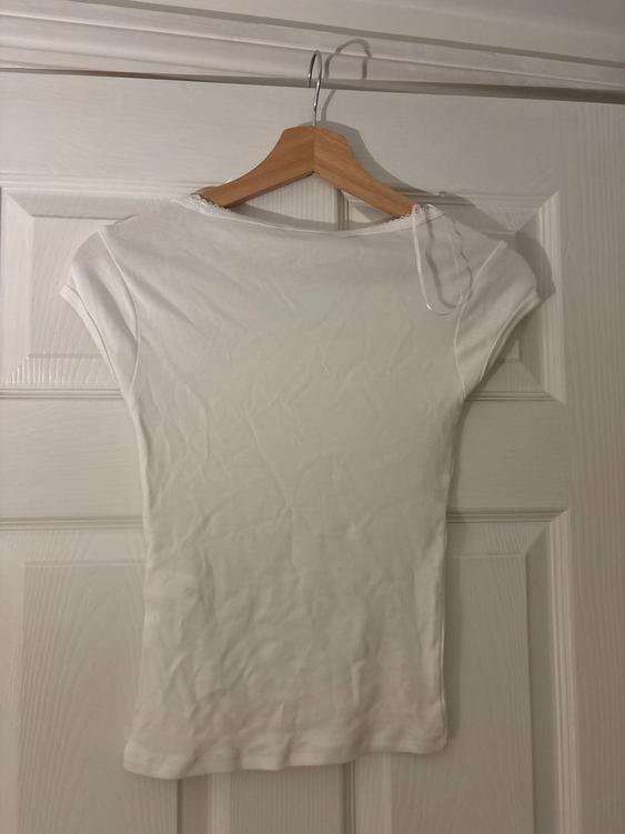 White short-sleeved t-shirt hanging on a wooden hanger over a white door. The fabric is slightly creased.