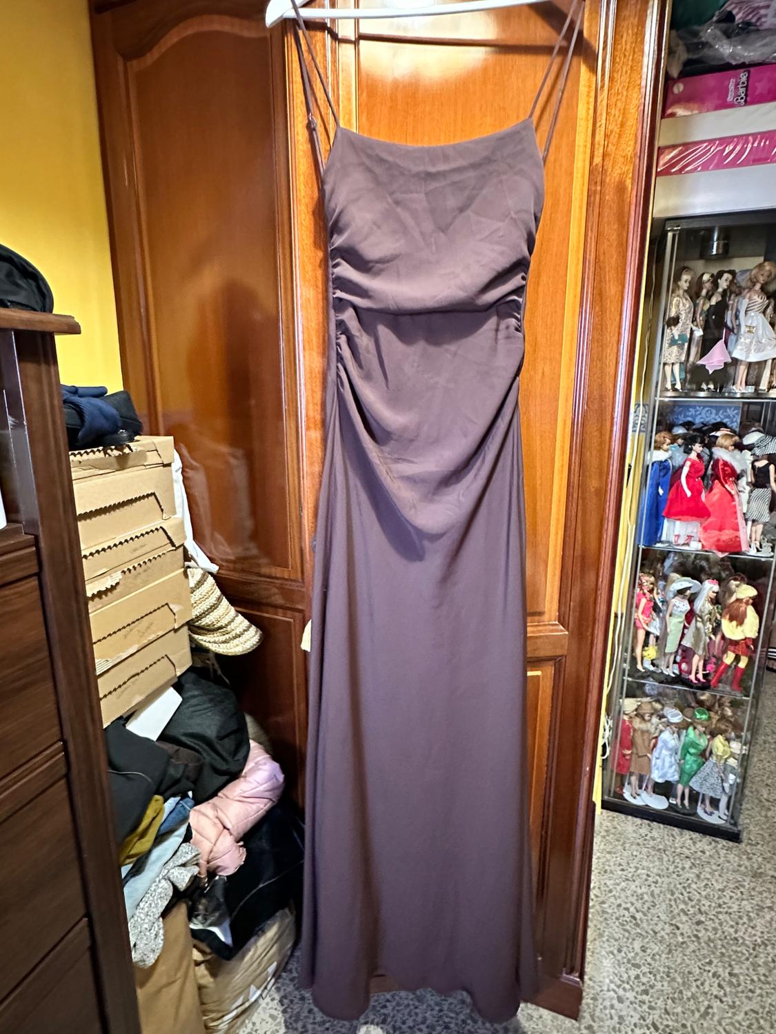 Plum-coloured strappy maxi dress hanging in a wardrobe. Room with boxes, clothes and a doll display cabinet. Visible text: Barbie.