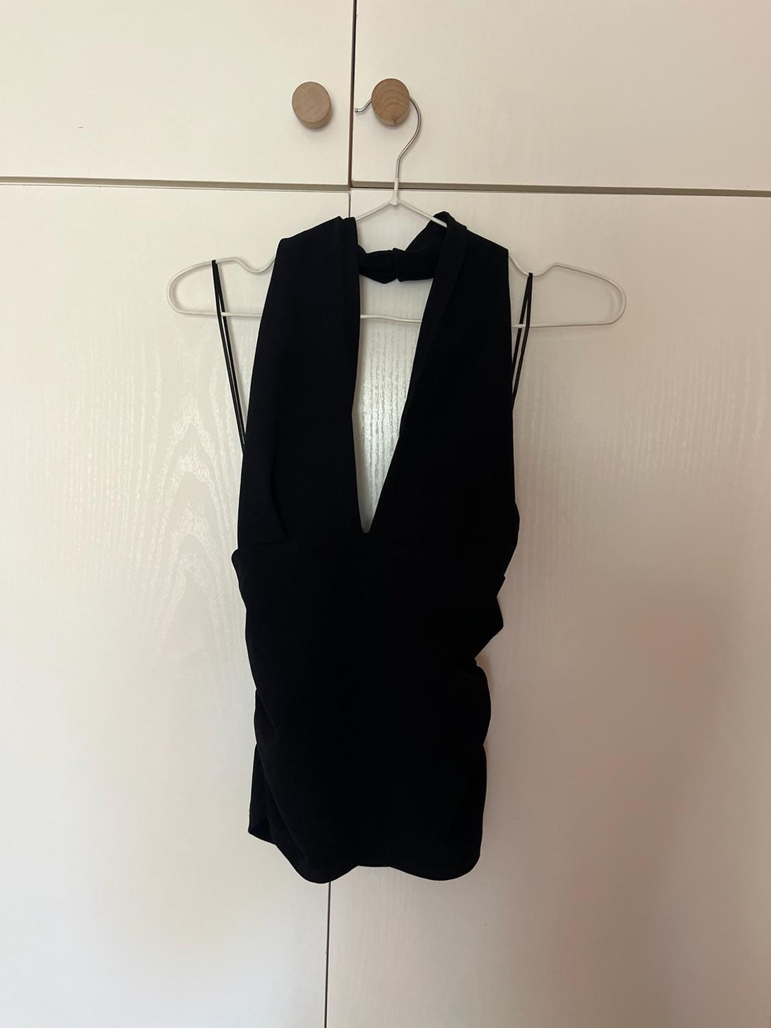 Black halterneck top with a deep V-neckline and ruched detail, hanging on a coat hanger above a white wardrobe.