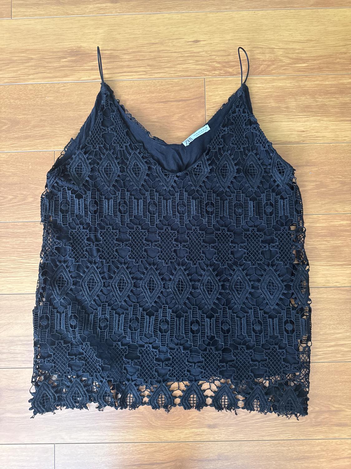 Black lace camisole with spaghetti straps on a light wood background. Geometric design and visible label inside.