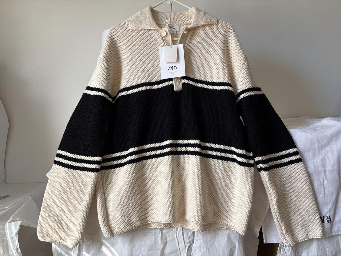 Beige knitted jumper with black and white stripes, hanging on a clothes hanger. Visible label with the text "ZARA".