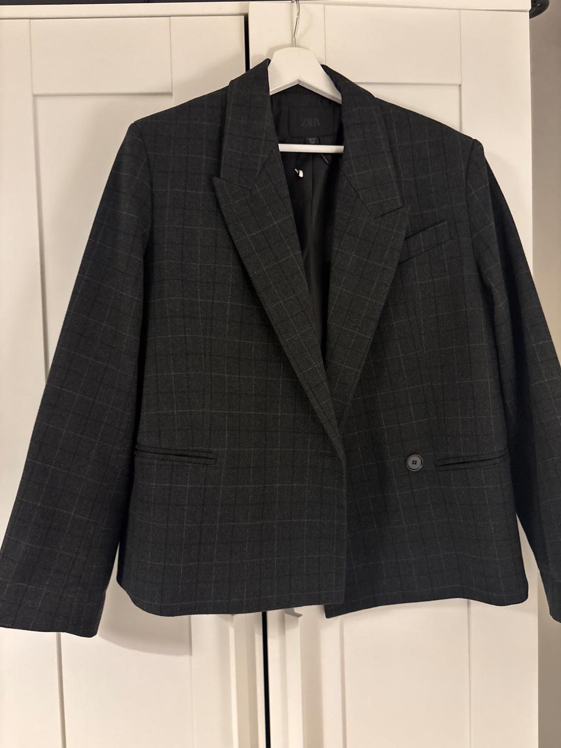 Grey checked jacket, hanging on a white hanger in front of a white wardrobe.