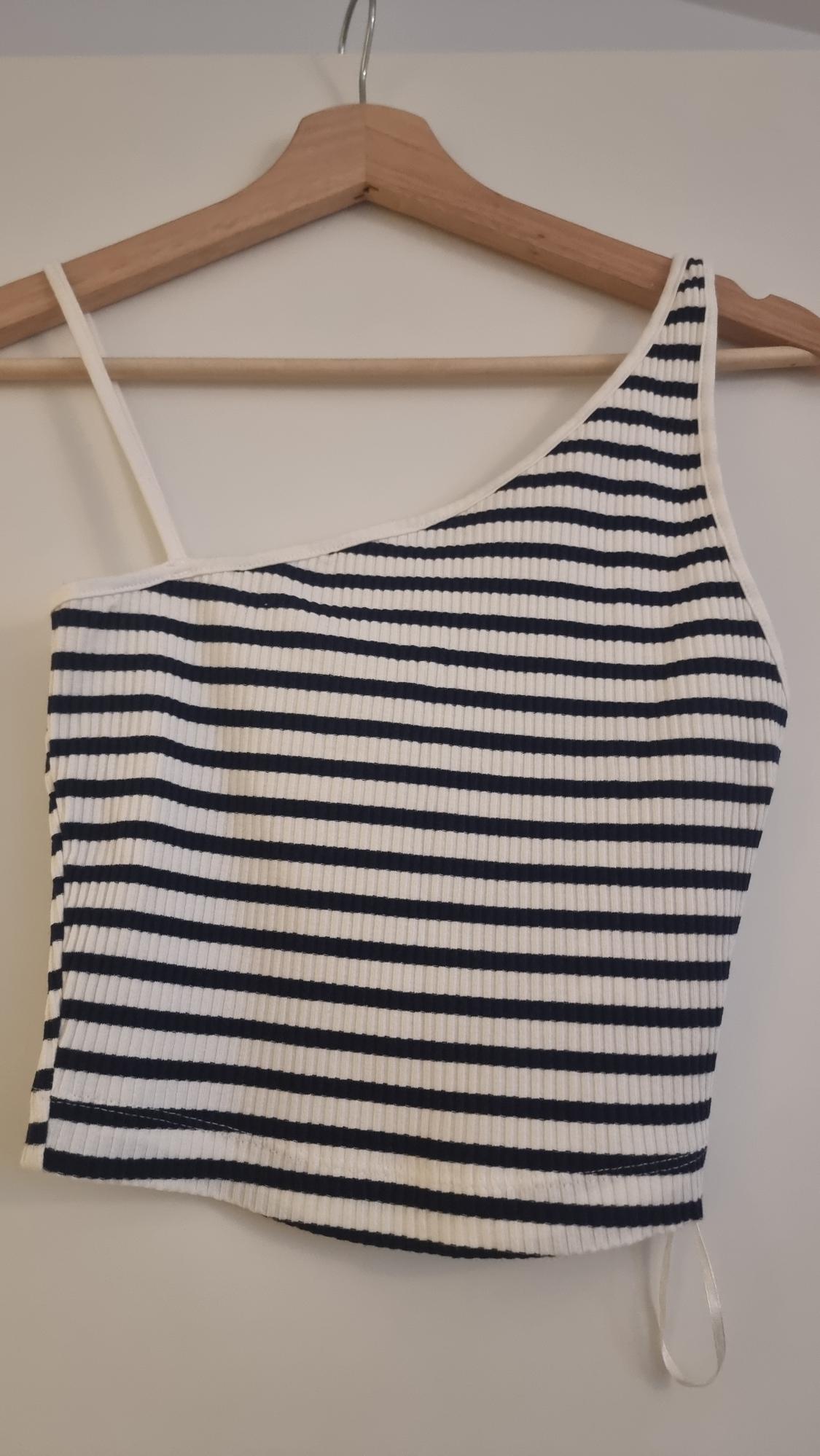 Asymmetric black and white striped camisole top hanging on a wooden hanger against a white background.