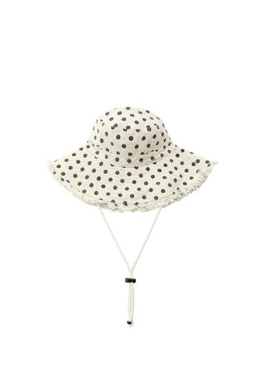 Light-colored bucket hat with black polka dot print, frayed edges, and adjustable drawstring, on a white background.