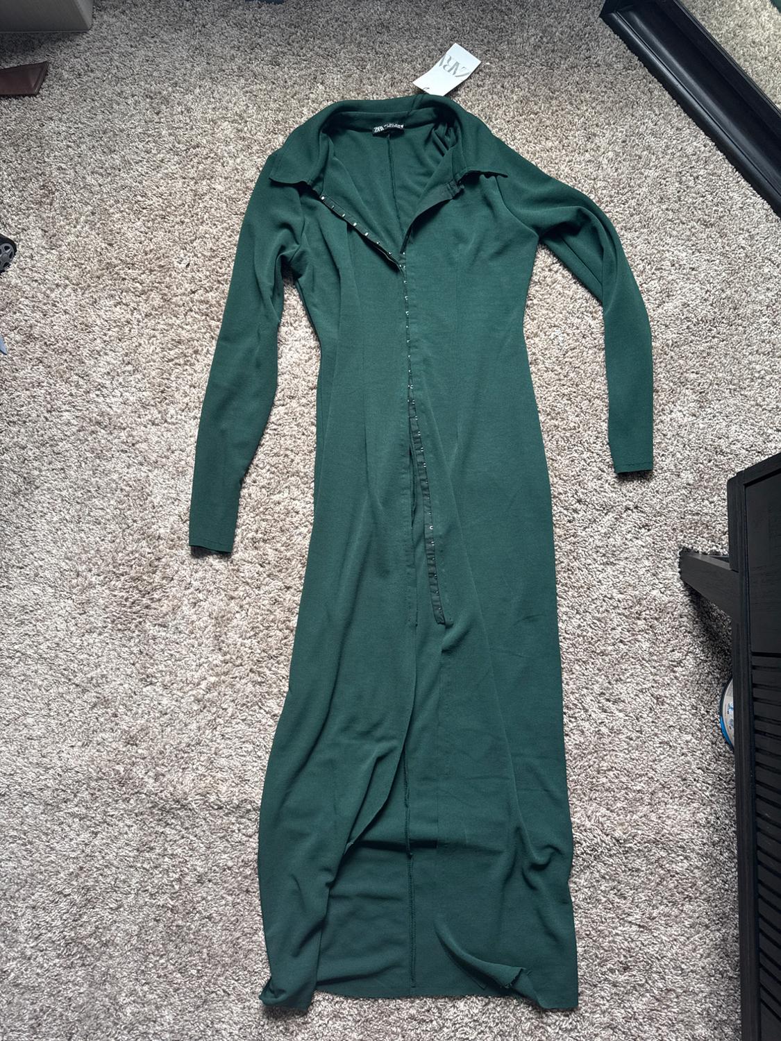 Long-sleeved green maxi dress with a collar and front button closure, laid out on a beige rug. Label with the text ZARA.