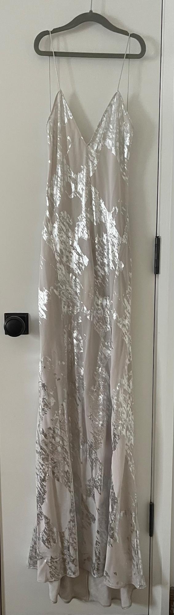 Long beige dress with a silver abstract print and thin straps, hanging on a hanger on a white door with a black knob.
