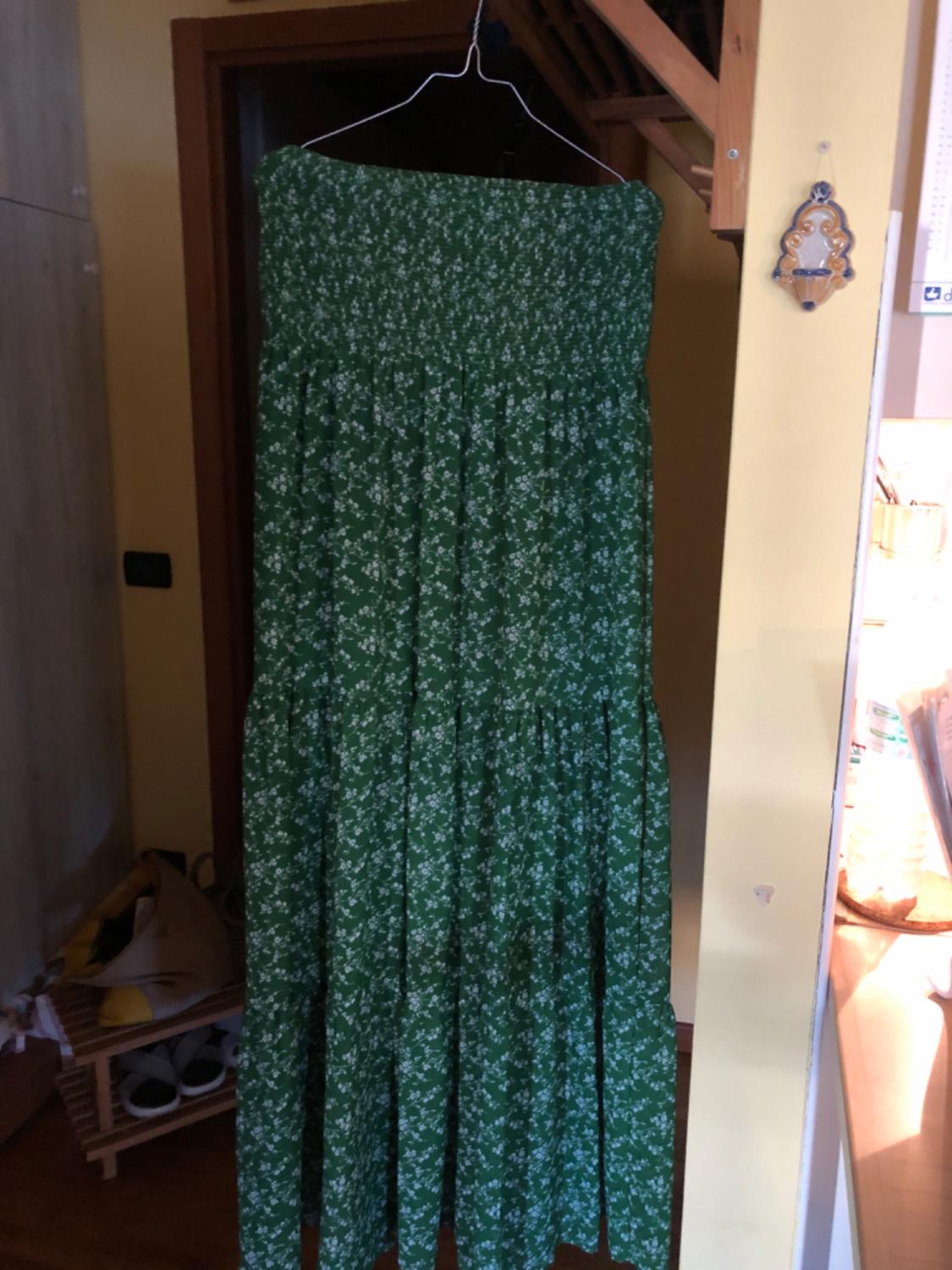 A long green dress with a white floral pattern hanging on a hanger inside a dimly lit room.