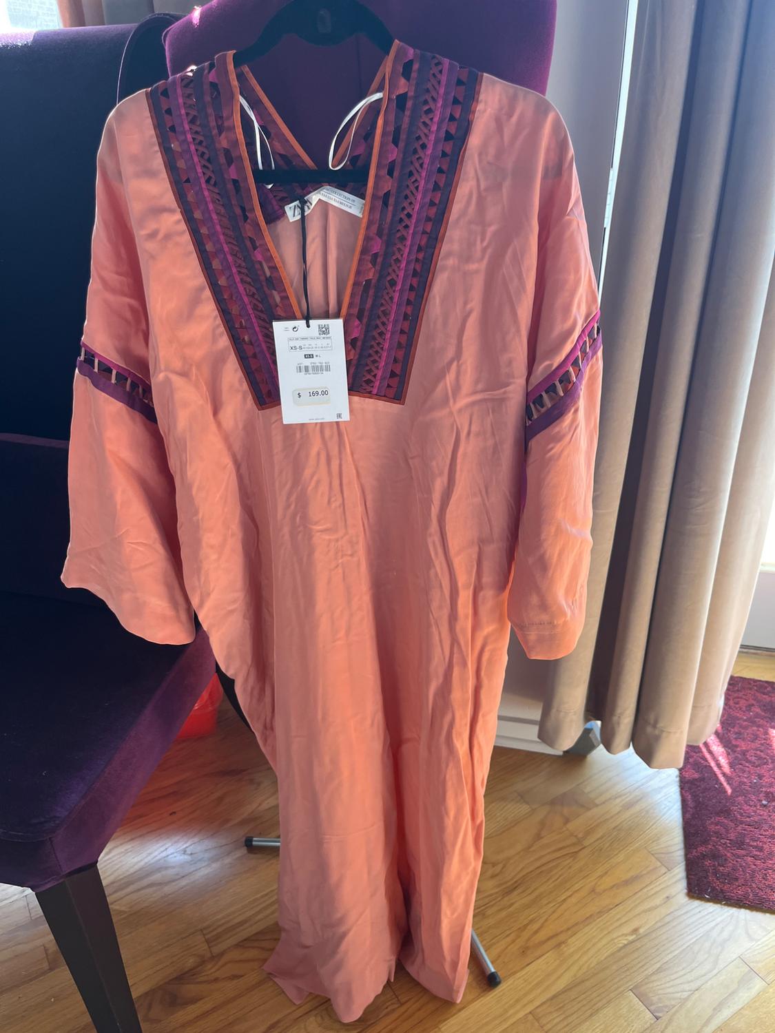 Orange maxi dress with geometric embroidery on the neckline and sleeves. Visible tag with price of $169. Hanging on a hanger.