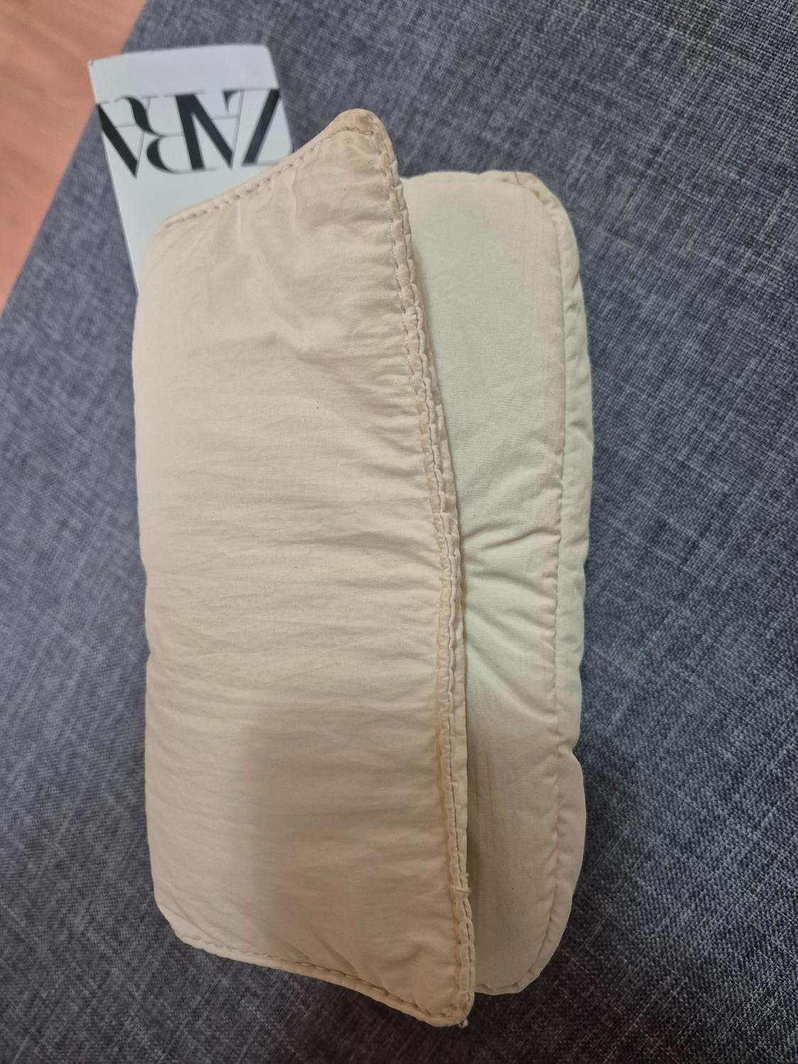 Quilted beige handbag on grey fabric, with visible label that says "ZARA". The design is simple and modern.