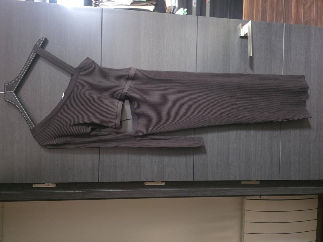 Dark grey ribbed knit asymmetric dress with cut-out details, hanging on a hanger against a wood panelled background.
