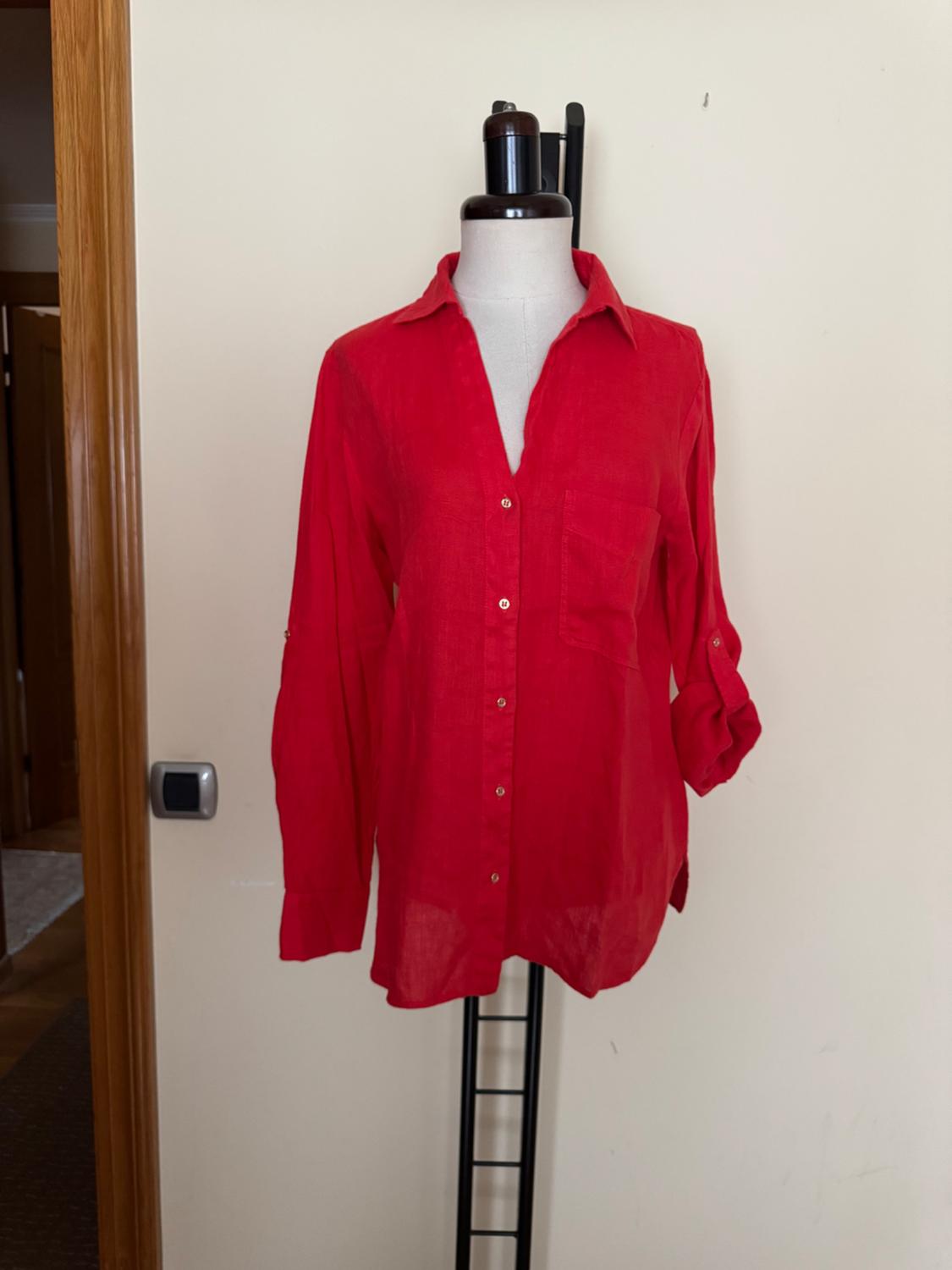 Long-sleeved red shirt on a mannequin, with buttons and a chest pocket, against a backdrop of a white wall and wooden door.