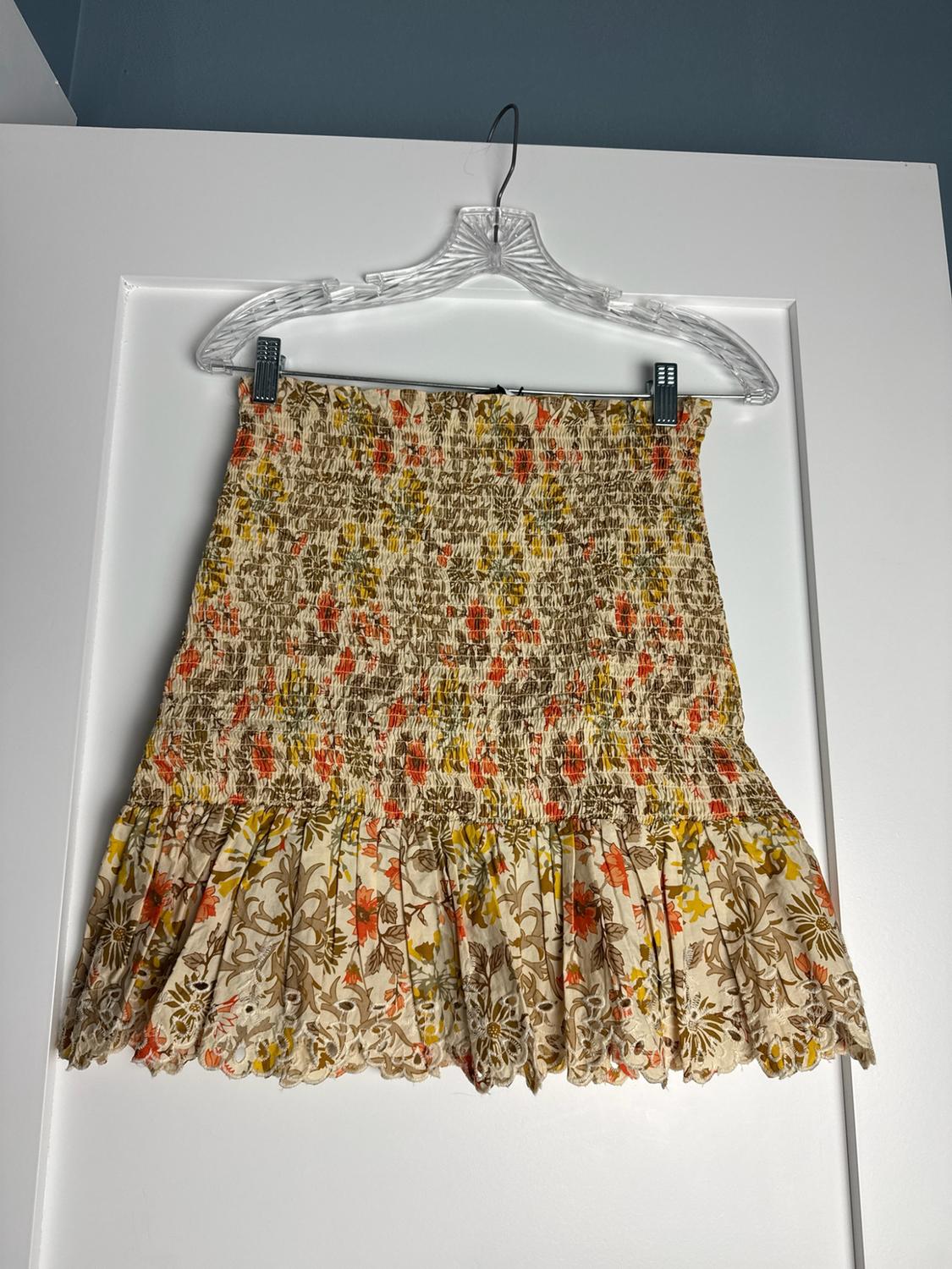 Short floral print skirt, gathered bodice and hem with broderie anglaise ruffle, hanging on a clear hanger over a white door.