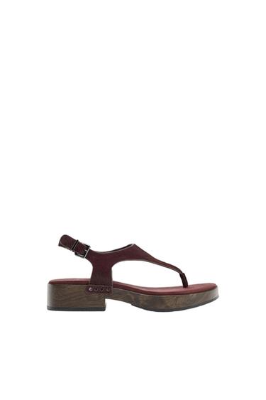 Brown sandal with low wooden heel and adjustable strap. Minimalist white background.