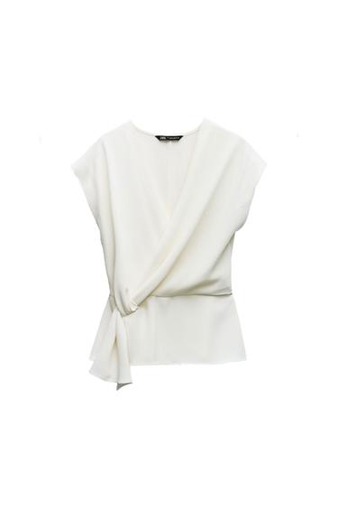 White sleeveless top with a V-neck and a wrap design with a knot detail at the waist on a white background. Label with ZARA text.
