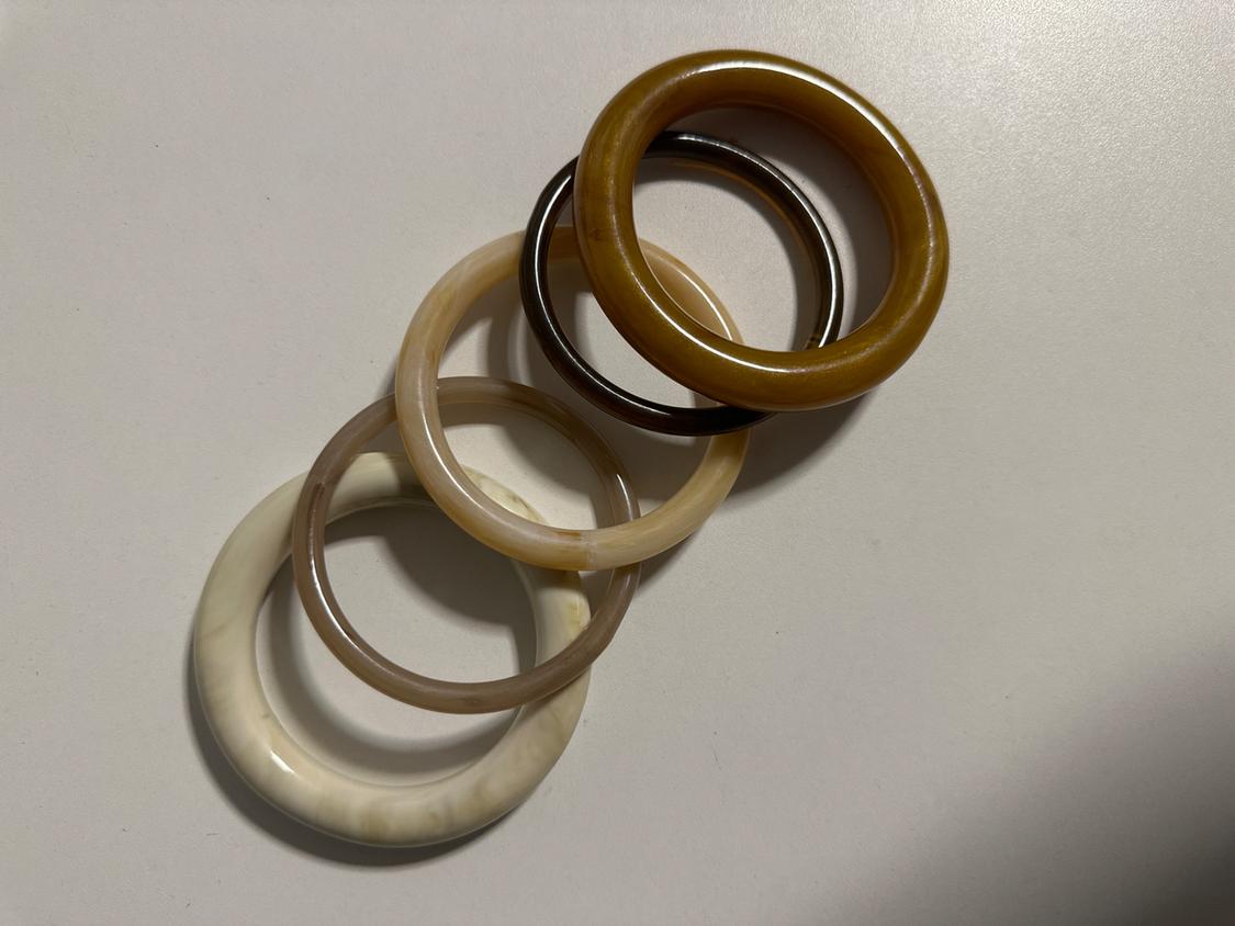 Five resin bracelets in earth tones, white, beige, brown, and mustard, layered on a white background.