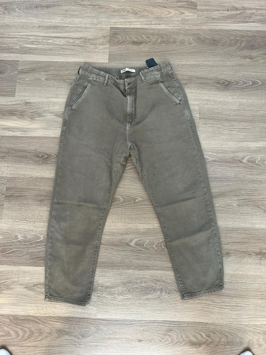 Olive green trousers on a light wood floor. They have pockets, an elasticated waist and an interior label with the text ZARA.