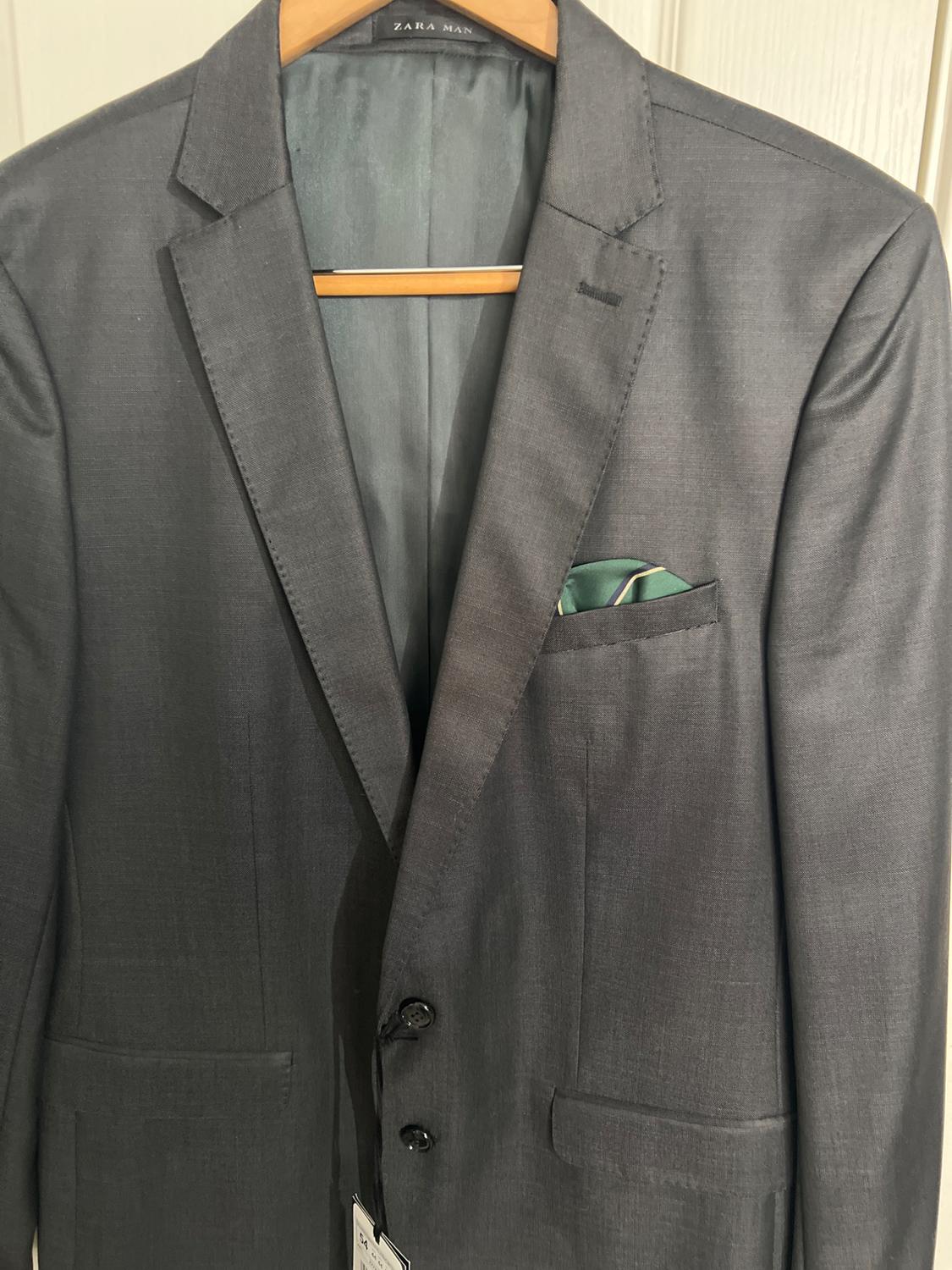 Dark gray suit hanging on a wooden hanger, with a green pocket square. Visible tag: "ZARA MAN".