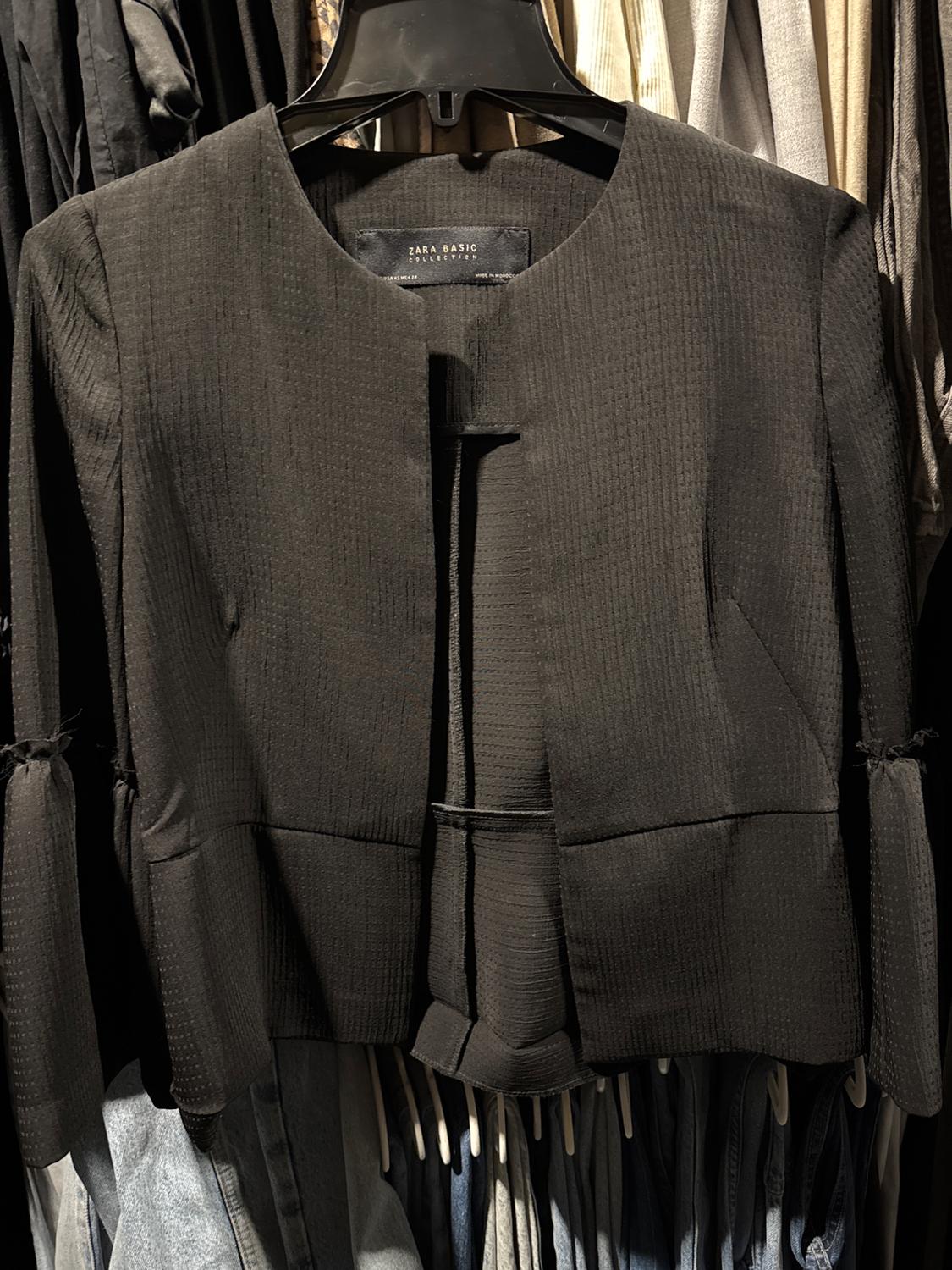 Front view of a black jacket with a round neck and side pockets.