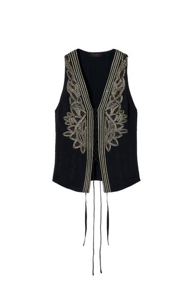 Front view of black vest with gold floral embroidery and hanging ribbons