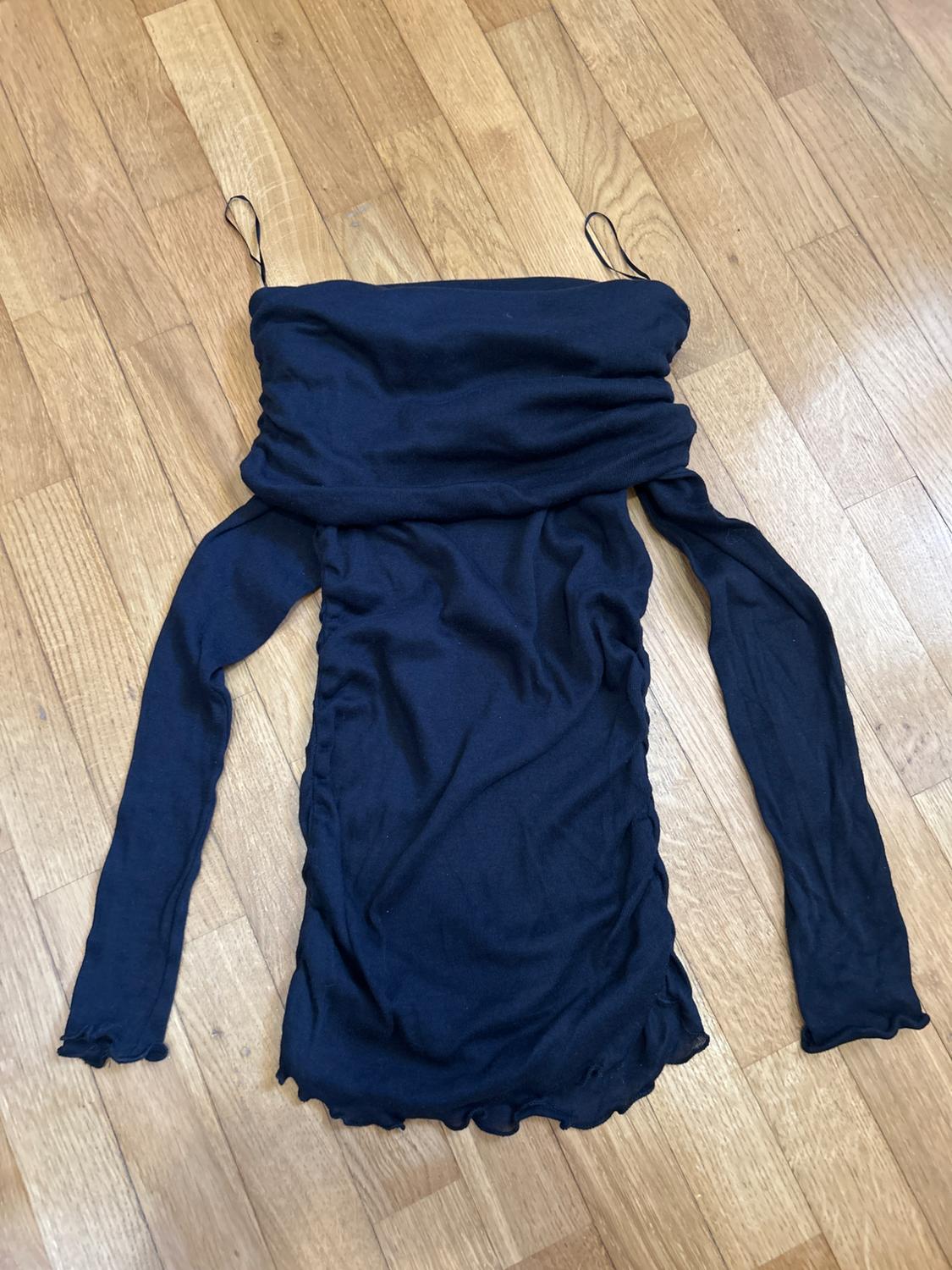 Navy long-sleeved top with a draped neckline, spaghetti straps, ruching, and wavy edges, on a wooden floor.
