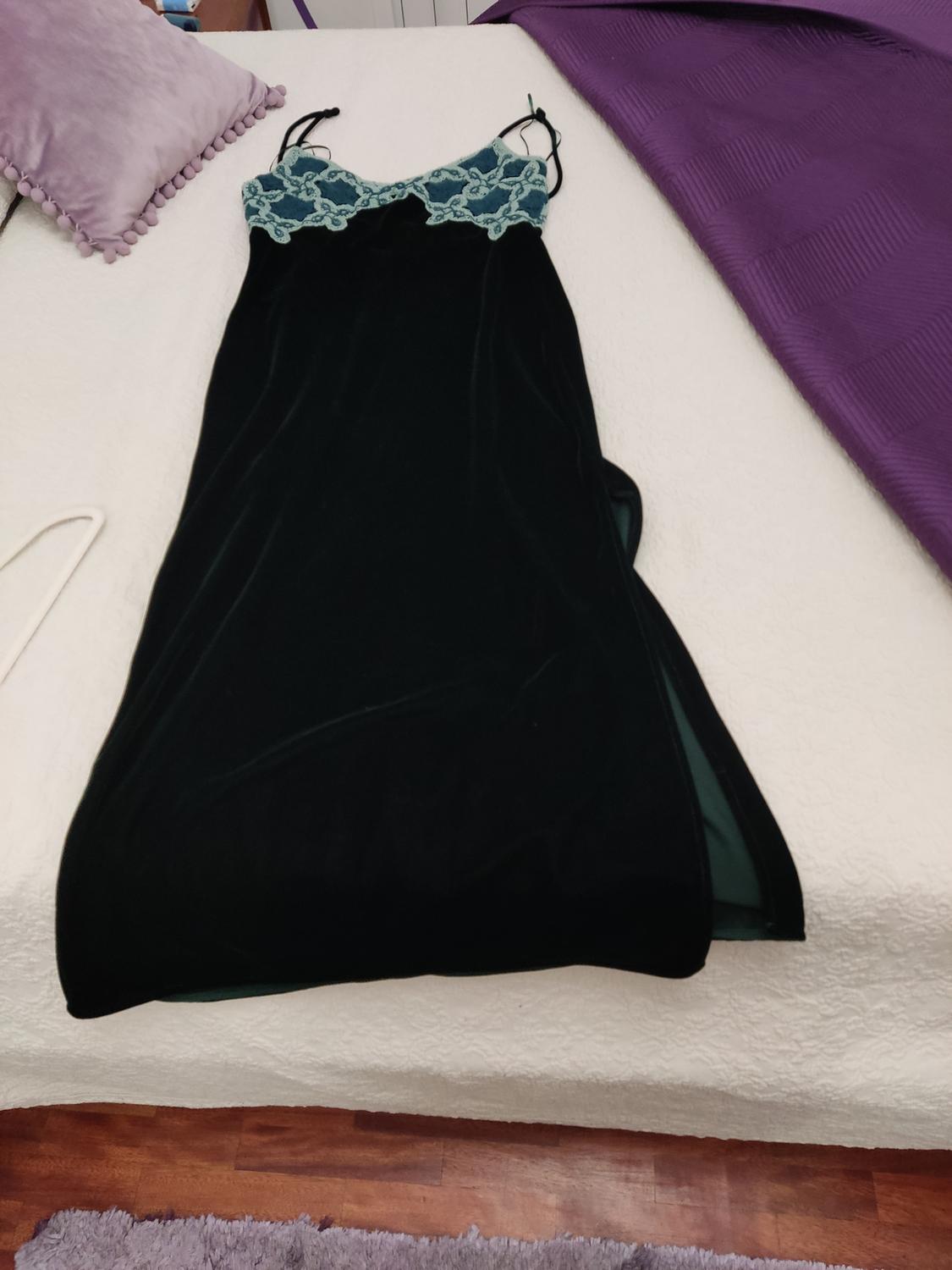 Black dress with blue lace on the top, on a white bed with a lilac cushion and a purple blanket.