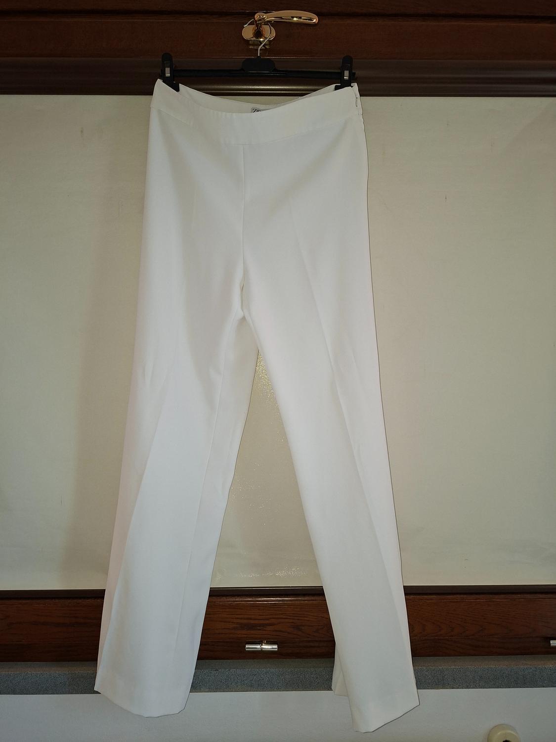White trousers hanging on a black hanger against a wooden background and light wall.
