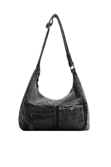 Front view of a black handbag with two front pockets, one with a zip and one with an adjustable drawstring, and an adjustable strap.
