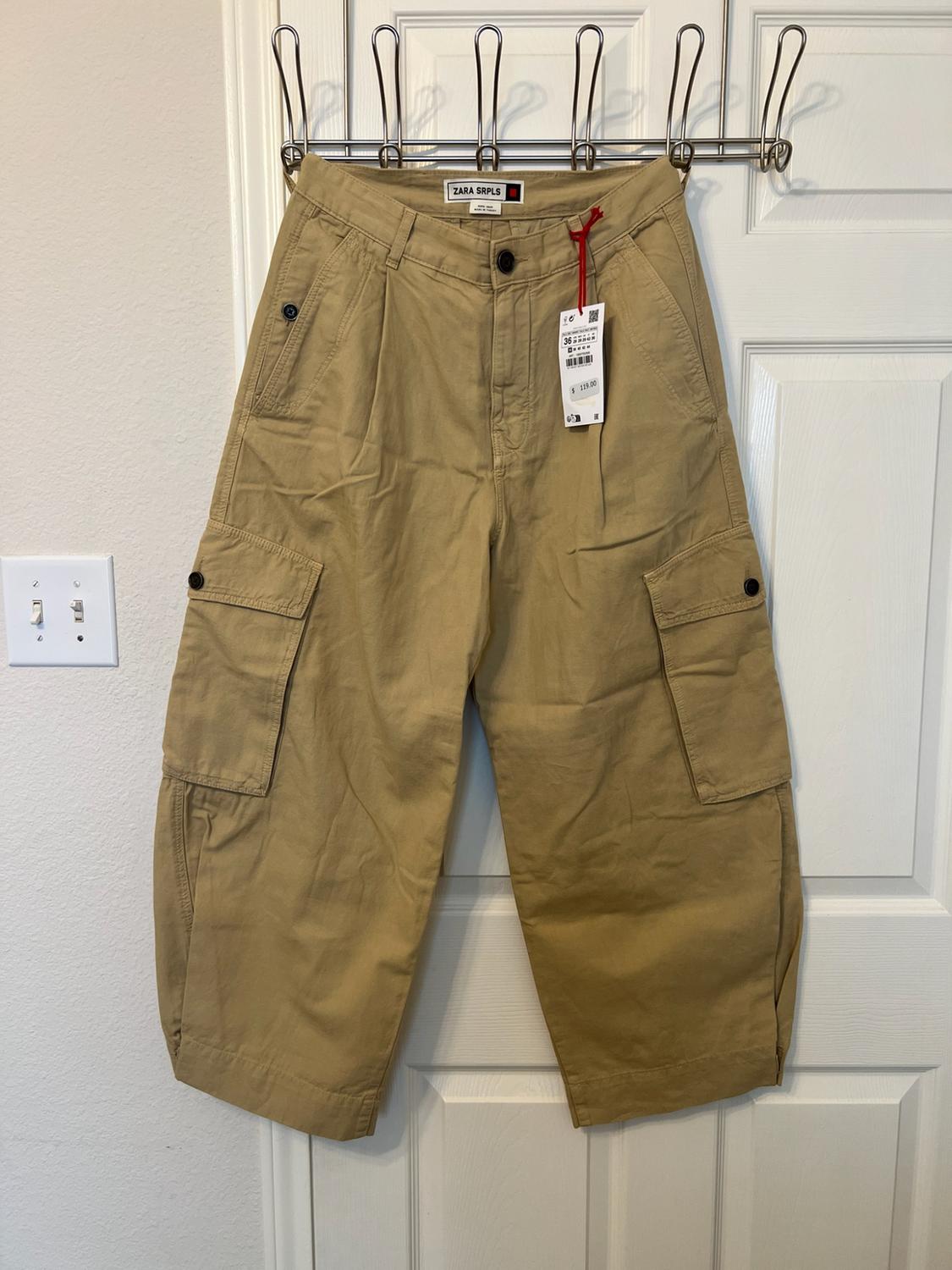Beige cargo trousers with side pockets, hanging on a white door. Inner label with the text ZARA SRPLS.