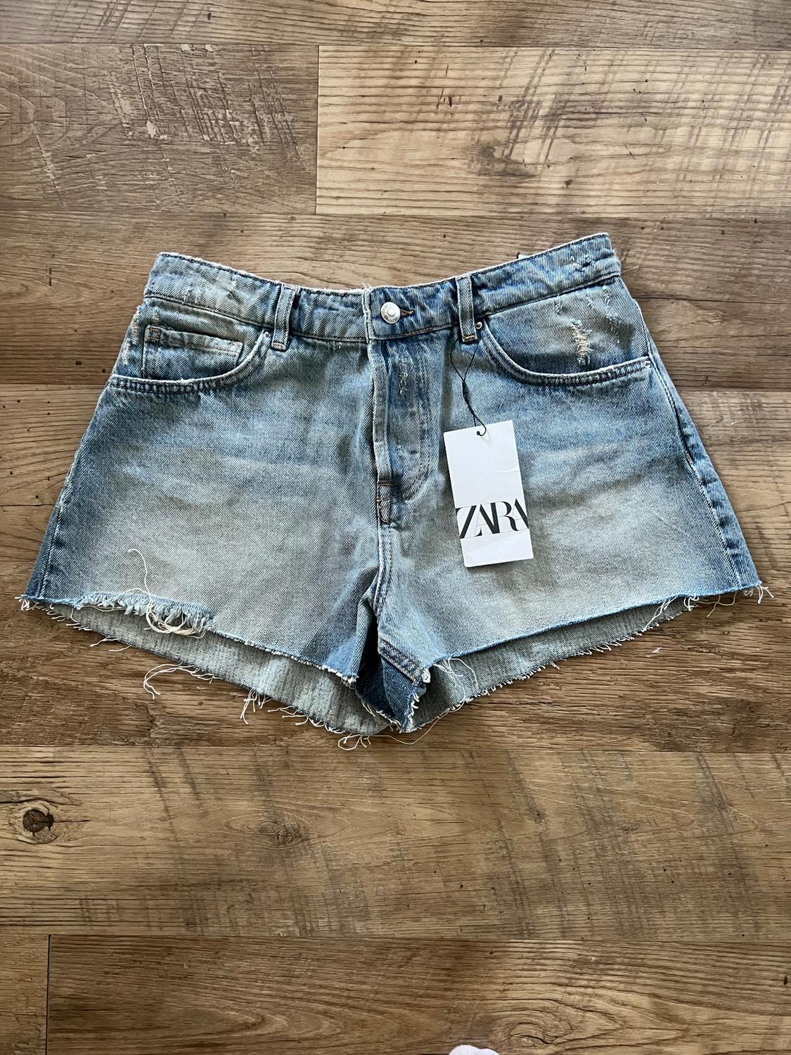 Distressed denim shorts with hang tag on a wooden floor.