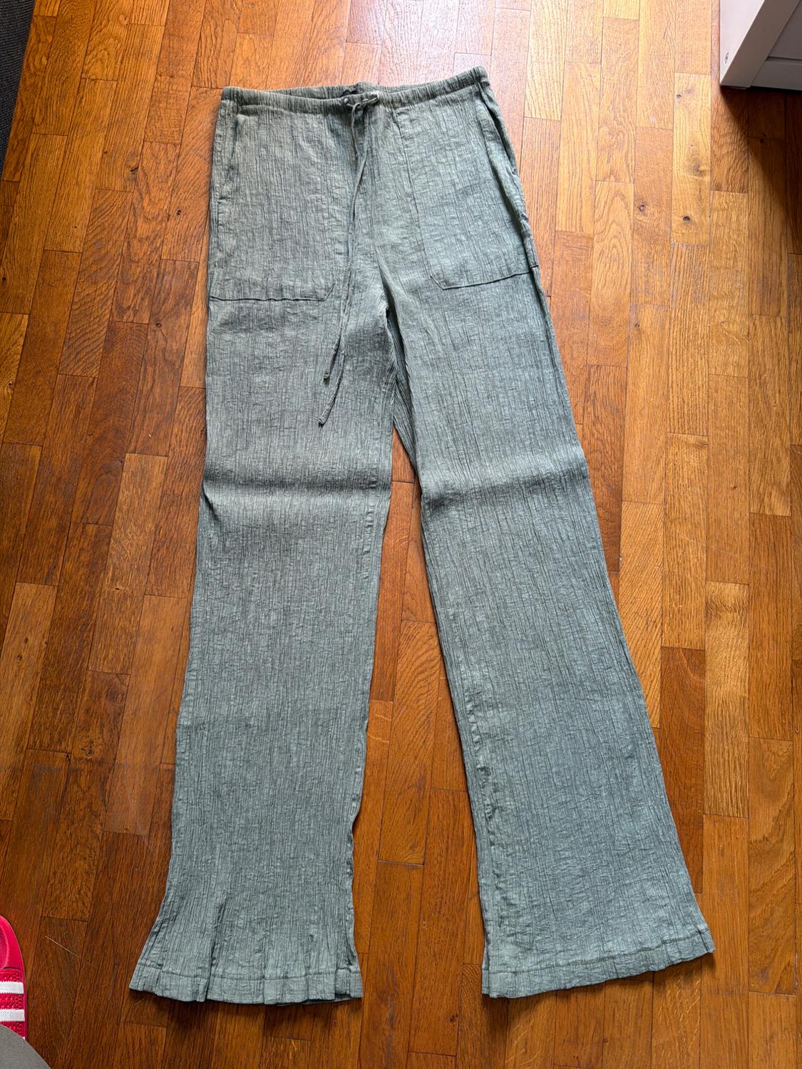 Light green textured wide-leg trousers with a drawstring waist and front pockets, on a wooden floor.