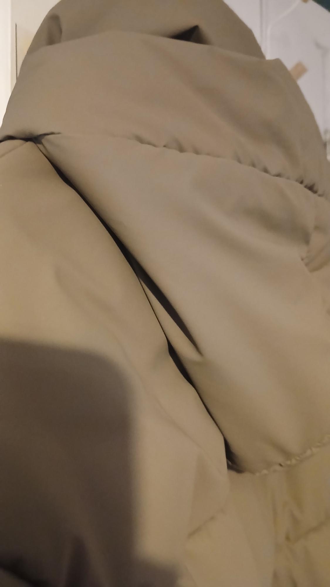 Detail of a beige quilted jacket, showing the seams and fabric folds in an indoor setting.