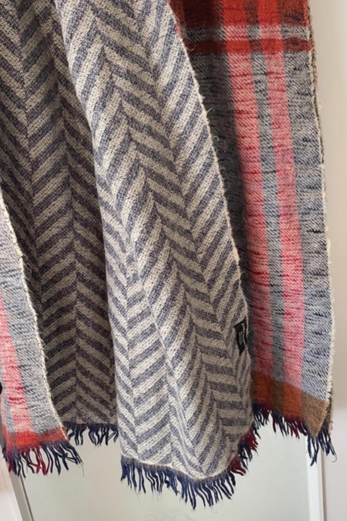 Detail of a blue and grey herringbone patterned scarf, with a red checked border and fringe.