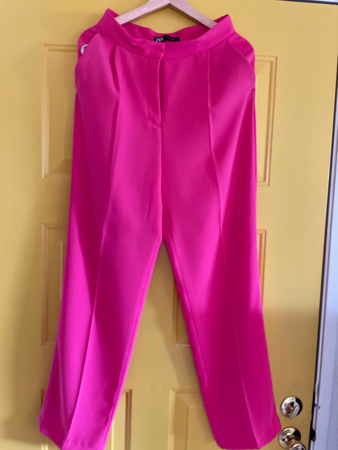 Fuchsia trousers hanging on a coat hanger over a yellow door.