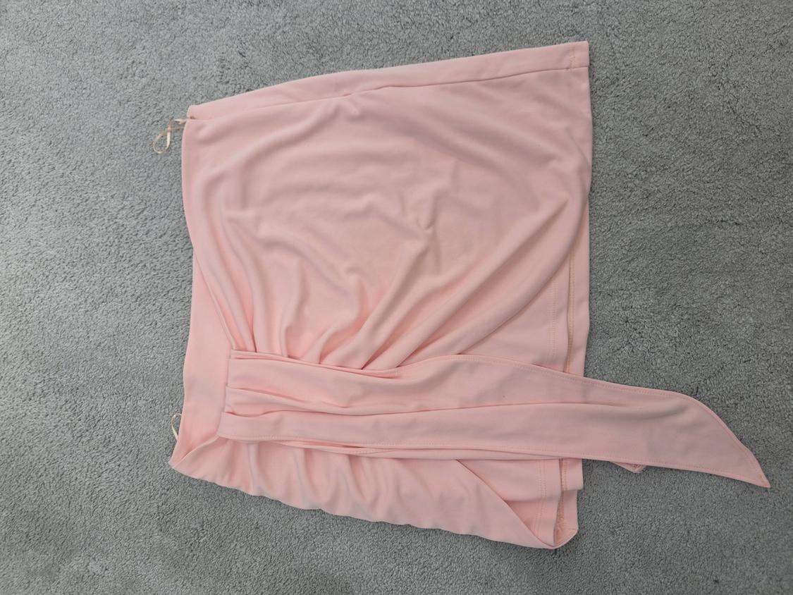 Light pink skirt with a draped design and belt, on a grey background.