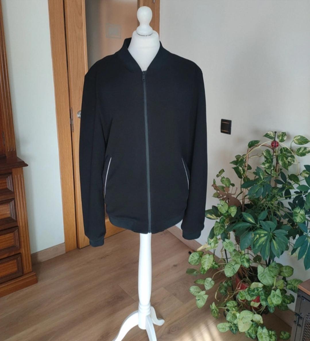 Front view of a black jacket with a zip and side pockets.