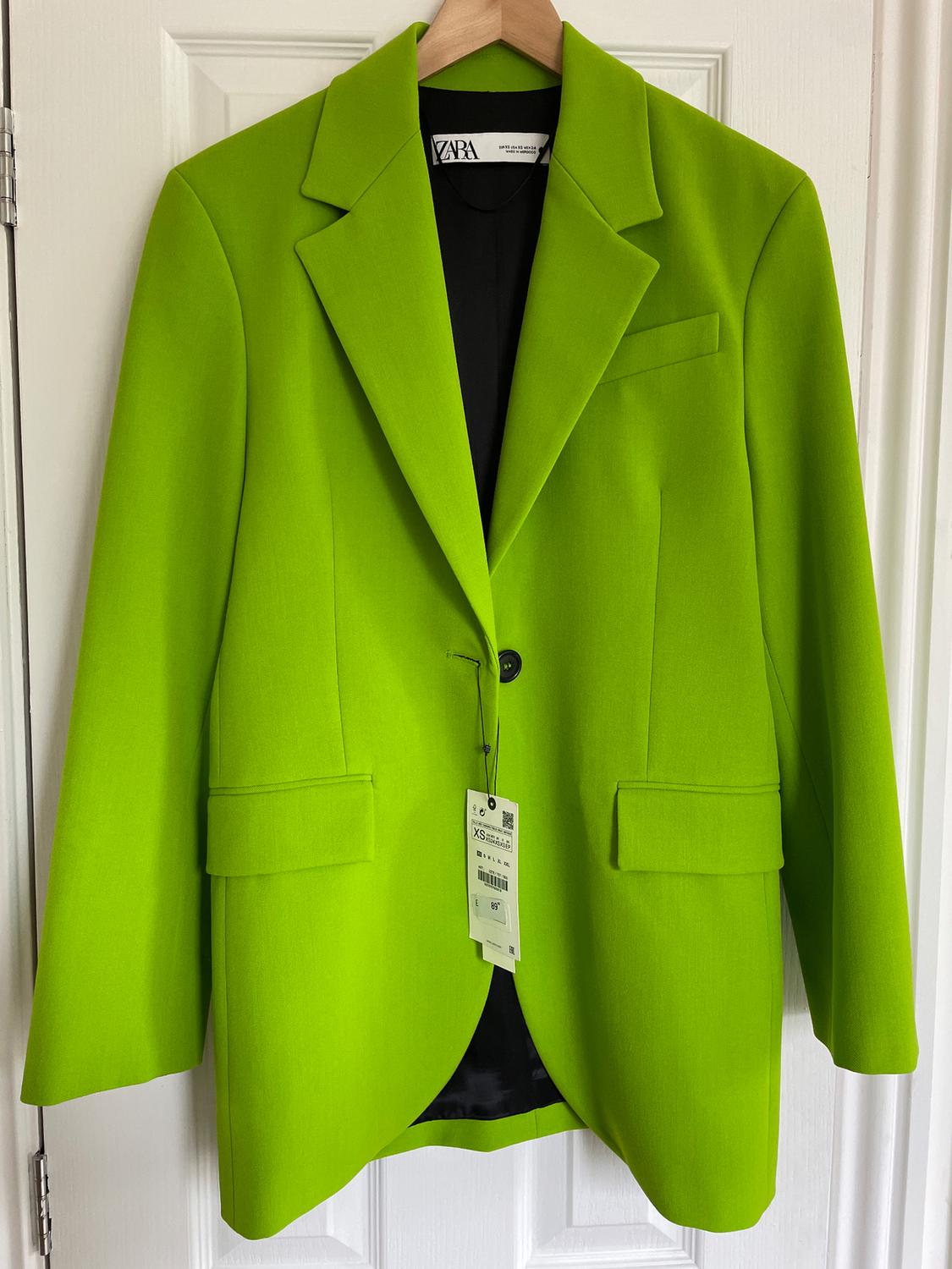 Bright green jacket hanging on a wooden hanger, with a visible XS size tag and brand label inside.