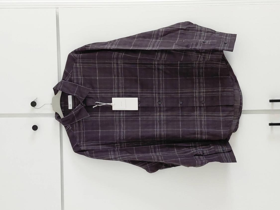Dark purple checked long-sleeved shirt with a label, hanging in a white wardrobe with black handles.