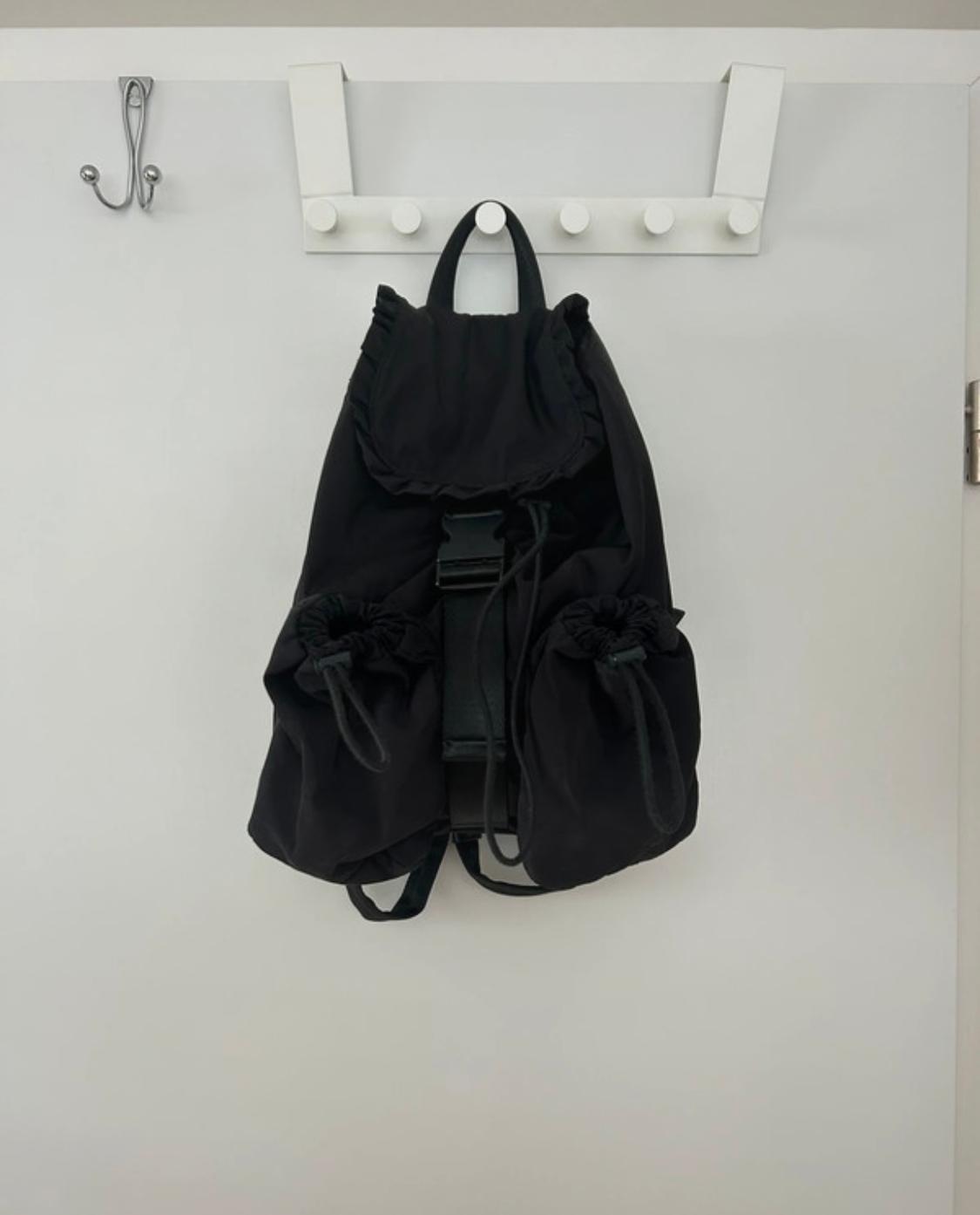Black rucksack hanging on a white coat rack with hooks. White background and minimalist setting.