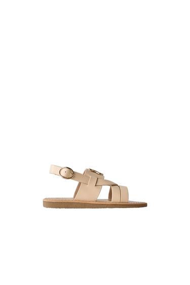 Side view of beige sandal with straps and gold buckle.