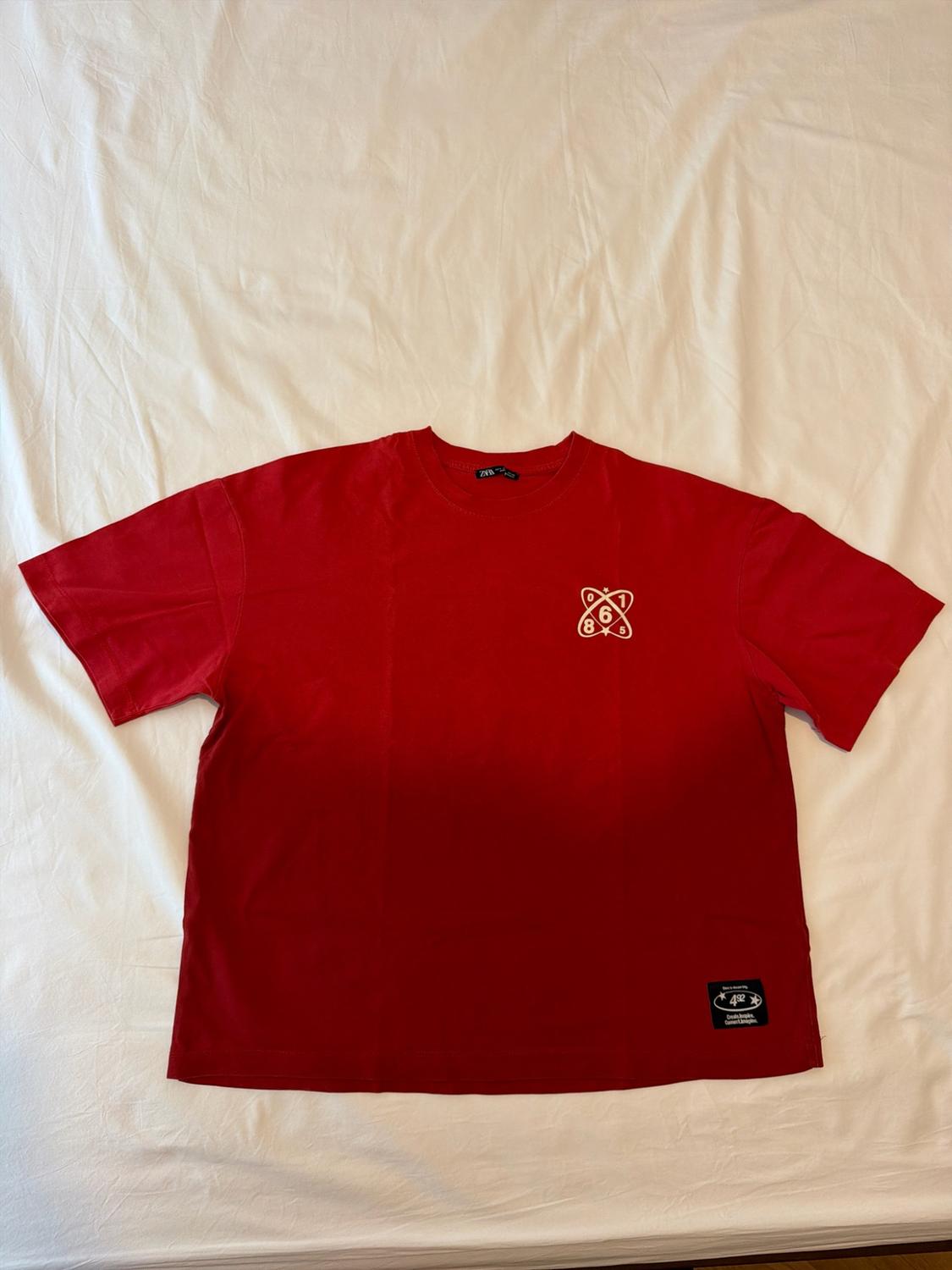 Red short-sleeved t-shirt on a white sheet. ZARA label. Graphic on the chest with 0 1 6 8 5 and a black patch at the bottom with 492.